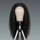Black curly wig on a mannequin head with a gray background