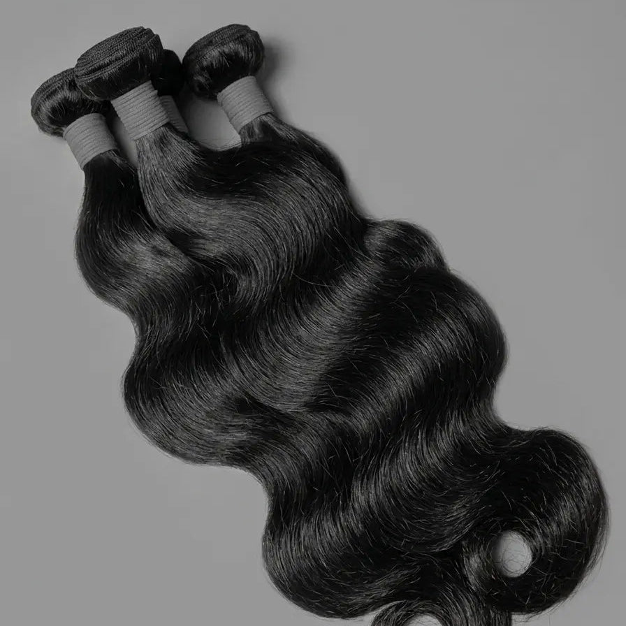 Three Brazilian body wave human hair bundles laid flat on a grey background